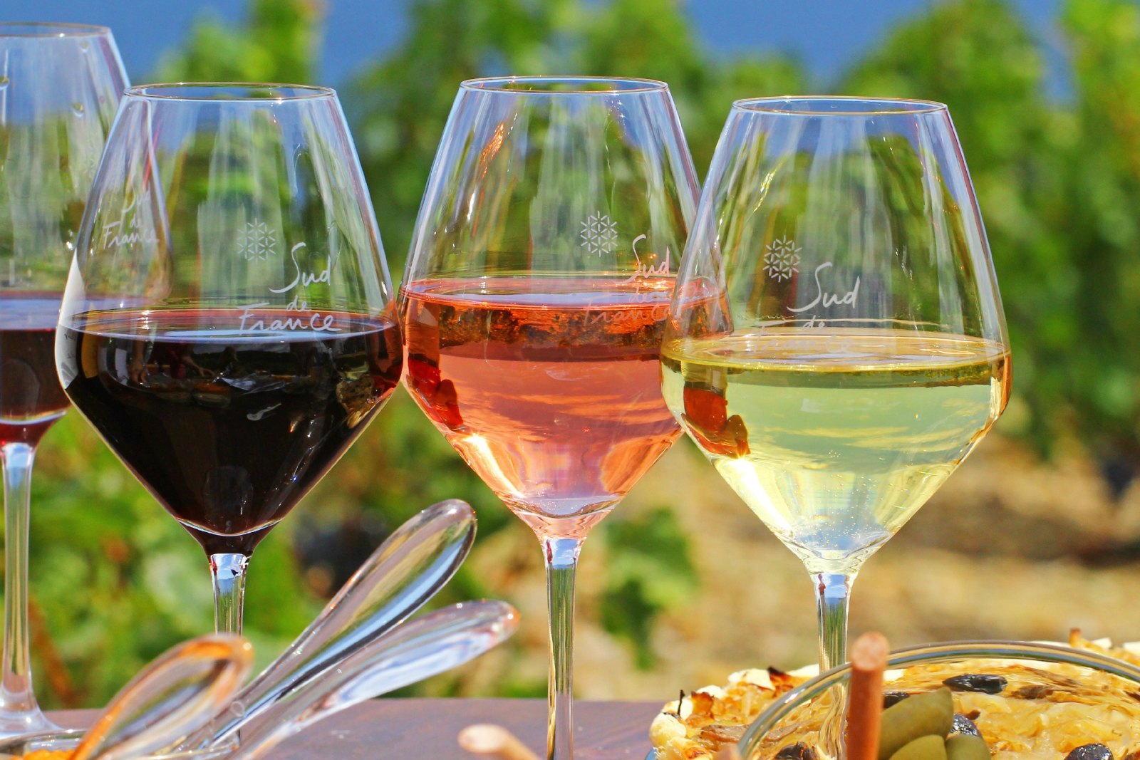 three glasses with Sud de France logo etched on them, one with red wine, one with white wine, one with ros&eacute;